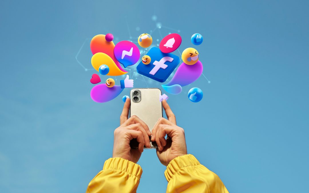 Hands holding a smartphone with colorful social media icons and emojis floating above against a blue sky.
